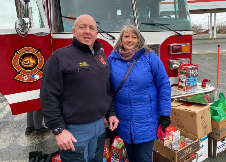 A firefighter poses with a woman in front of a firetruck.