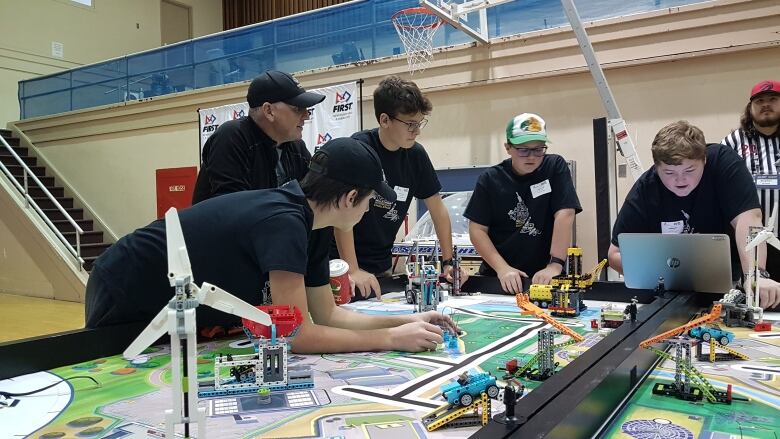 A group of students lean over a laptop computer and a table of Lego robots they have built, attempting to strategize for the forthcoming competition.