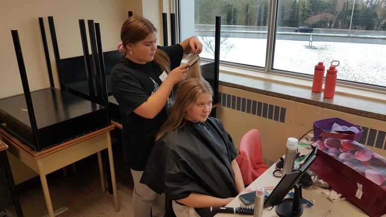 A young girl does her sister's hair in a classroom during a competition in hair styling.