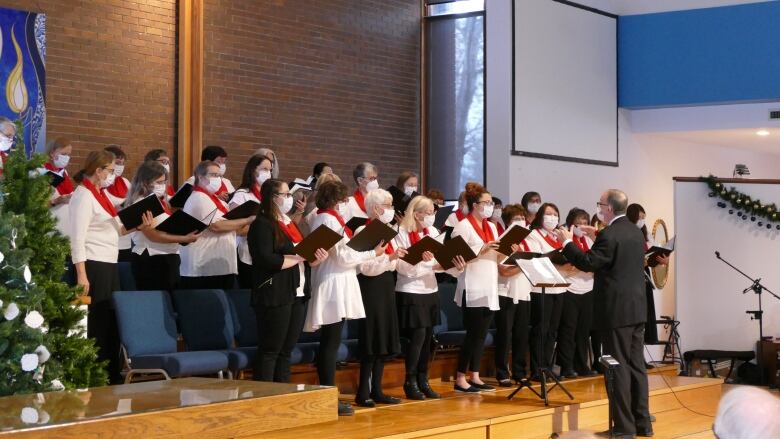 A choir of people in masks stand in front of a conductor.