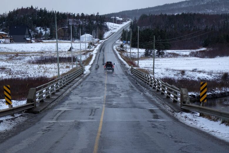 A truck crosses a two-lane bridge leading to a snow covered area.