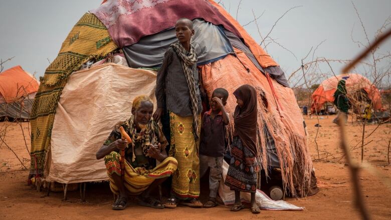 Four people stand outside of a hut in an arid landscape