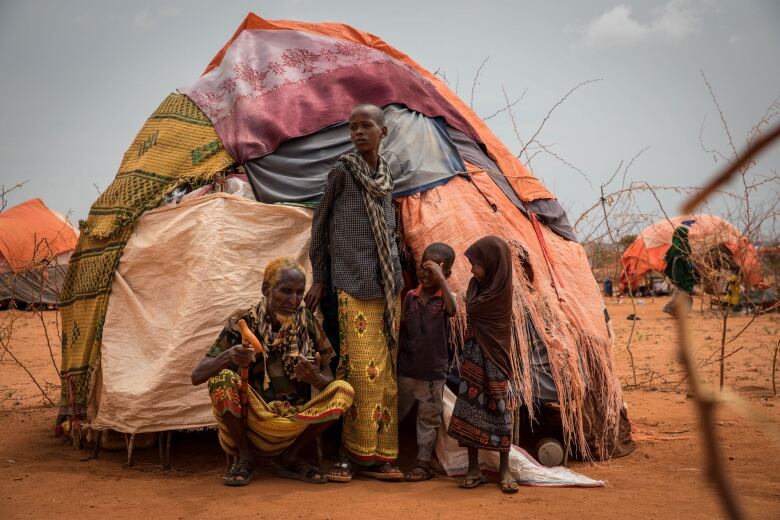 Four people stand outside of a hut in an arid landscape