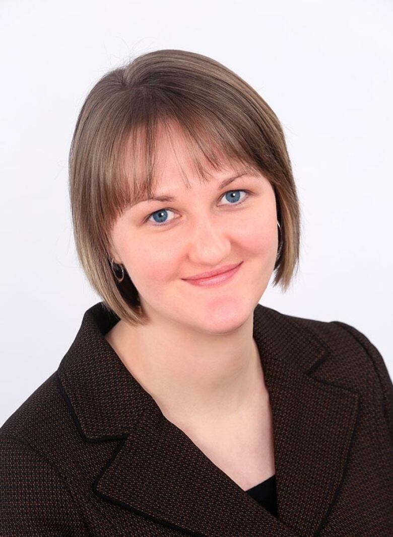 A vertical shot of a person wearing a brown blazer smiles in front of a white background.