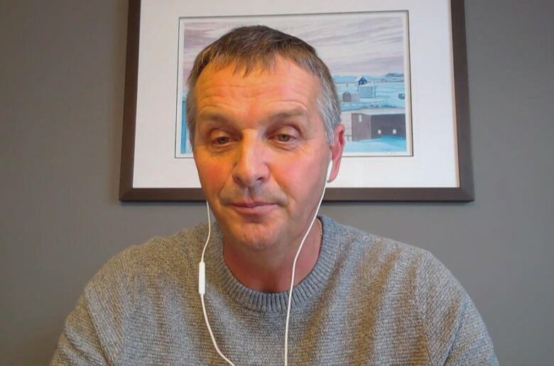 A chest-up shot of a person wearing a grey sweater and white wired headphones.