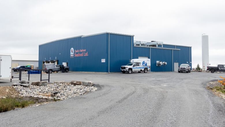 A large blue building with white and blue trucks is seen at the end of a gravel drive