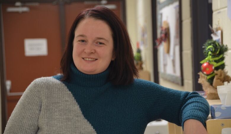 Heather Harris wears a grey and green sweater, leaning on a shelf with Christmas decorations behind her. 