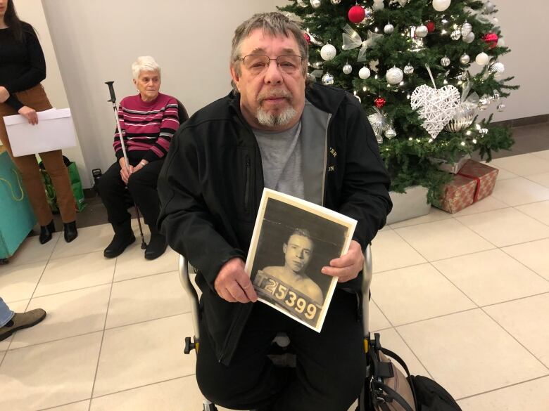 A man in a wheelchair holding a black and white photo of his father as a young man.