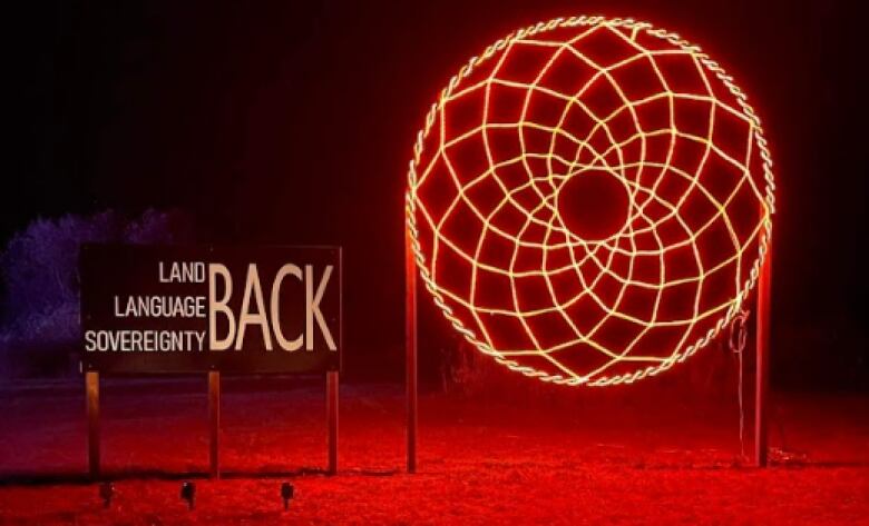 Large illuminated dreamcatcher with a sign on the left written land, language, sovereignty back