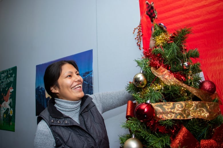 A woman decorates a Christmas tree while smiling.