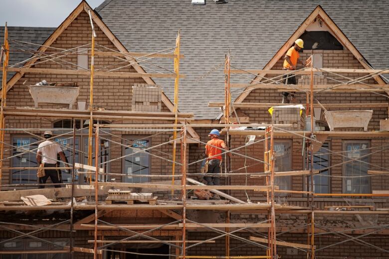 Construction workers on scaffolding in front of new housing build