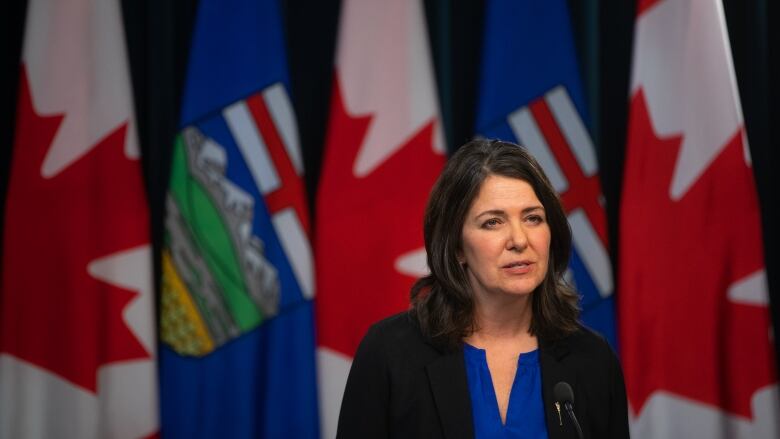 Alverta Premier Danielle Smith addresses media at a podium with Canadian and Alberta flags behind her.