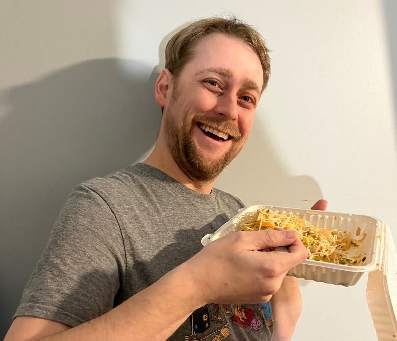 Man, looking happy, eats takeout food from a disposable container.