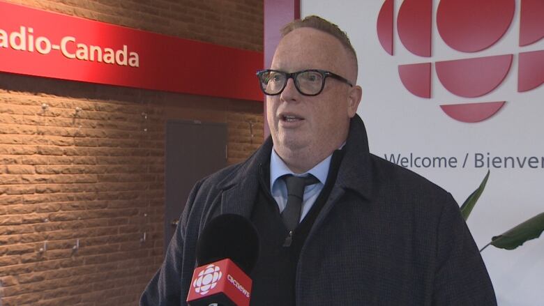 A man with glasses speaks in front of a microphone in the CBC St. John's newsroom.