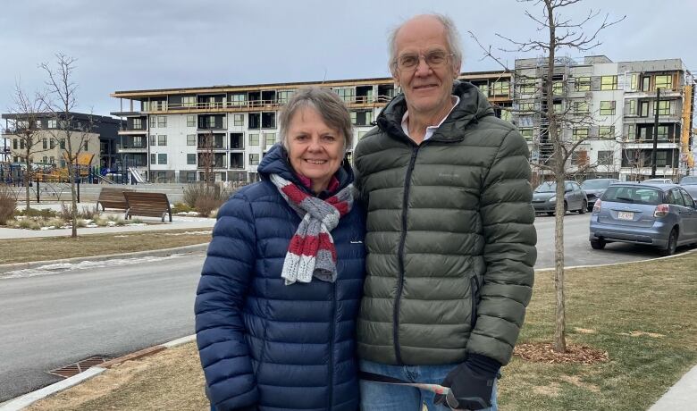 A couple stands with their dog in front of a condo building. 