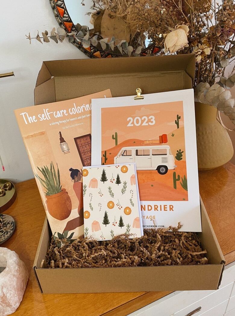 Photo of an open cardboard box filled with an illustrated notebook, colouring book and 2023 calendar.