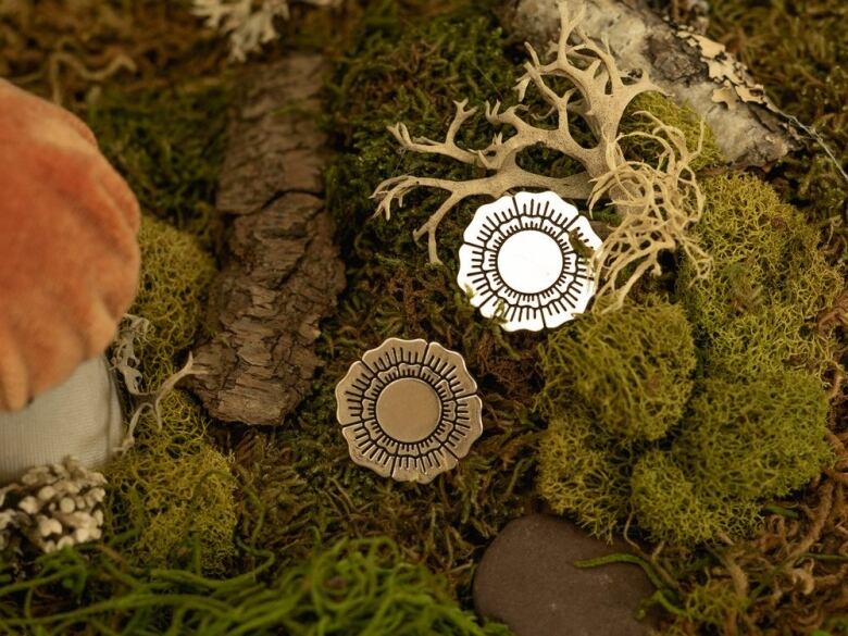 Photo of two silver metallic flower-shaped pins resting on a bed of green moss.