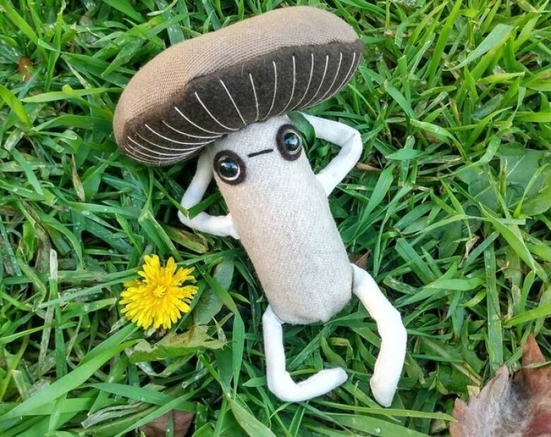 Stuffed figure of a cartoon portobello mushroom, reclining on the grass.