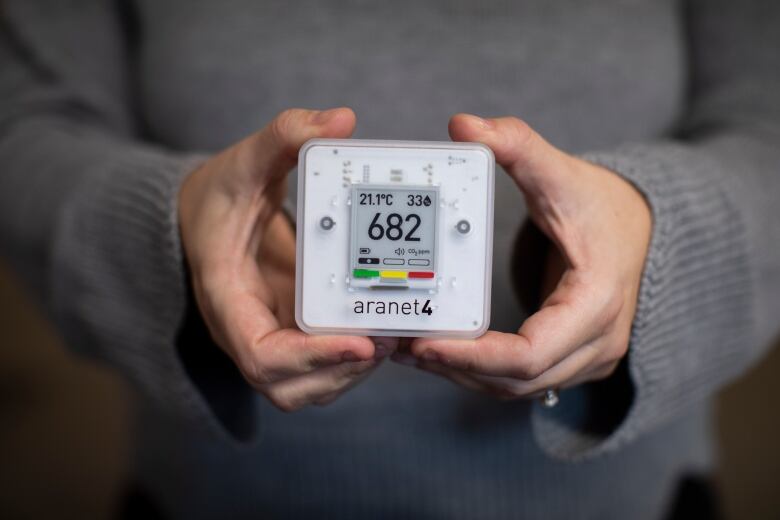 A person holds up a portable device with the reading '682', signifying carbon dioxide concentration in parts per million.