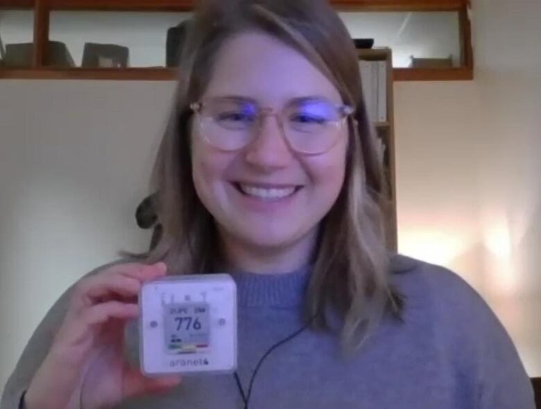 A blonde woman holds up a tiny device with numbers on its face.