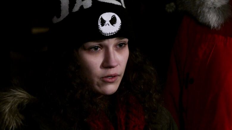 A young woman in a knit hat speaks with tears in her eyes.