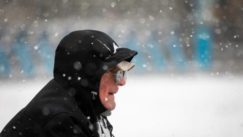 An old man walks through snow, with his glasses completely covered with powder.