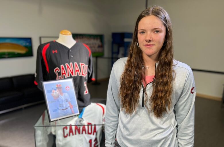 A young woman stands beside a display case with baseball jersey's and a portrait on top of it.