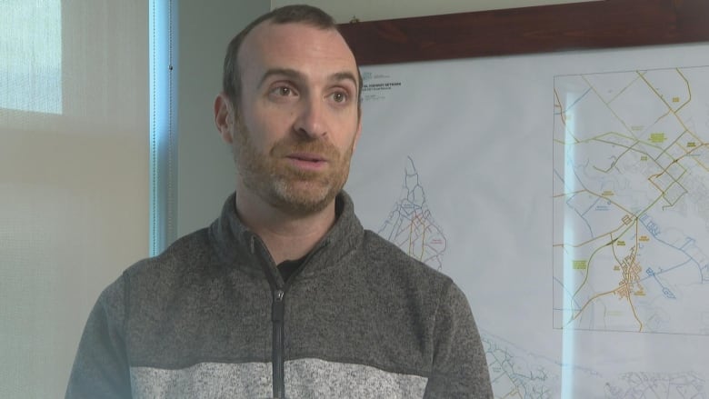 Bearded man in fleece jacket stands in front of a provincial map. 