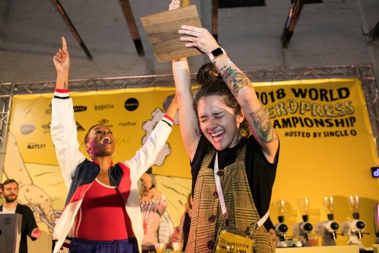 A white woman holds up a trophy in celebration as others cheer.