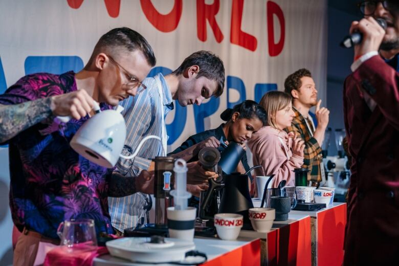 A row of people pour water into coffee mugs.