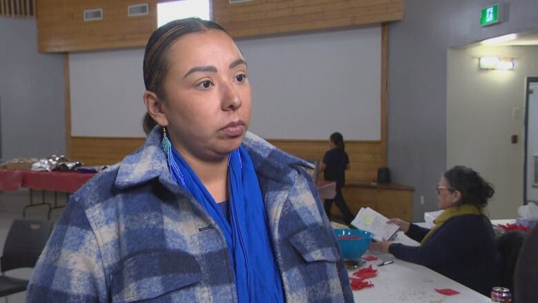 A woman in a blue plaid coat speaks to a person off-camera.