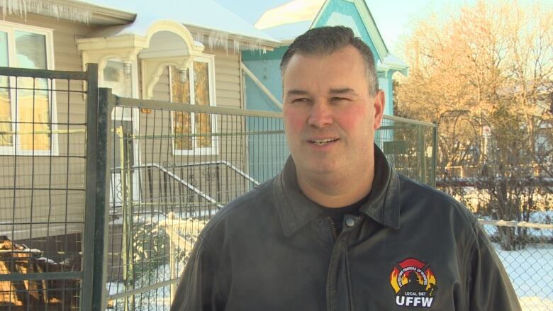 A man in short grey hair stands outside in winter, in front of a fenced-off property