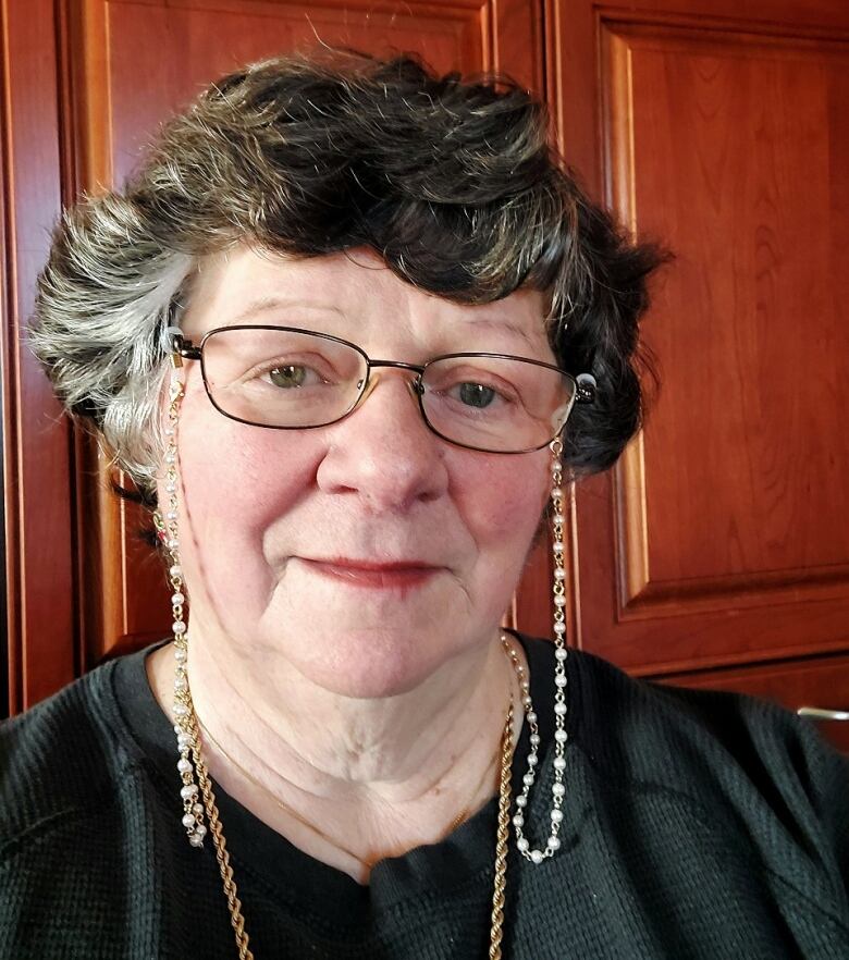 A white woman is seen with glasses on a long chain