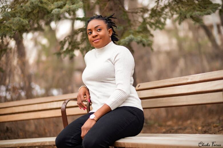 A woman wearing a white turtleneck sweater sits on an outdoor bench.