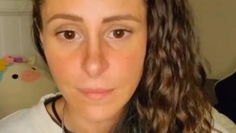 A woman with wavy brown hair looks at the camera with a serious expression in a social media video capture