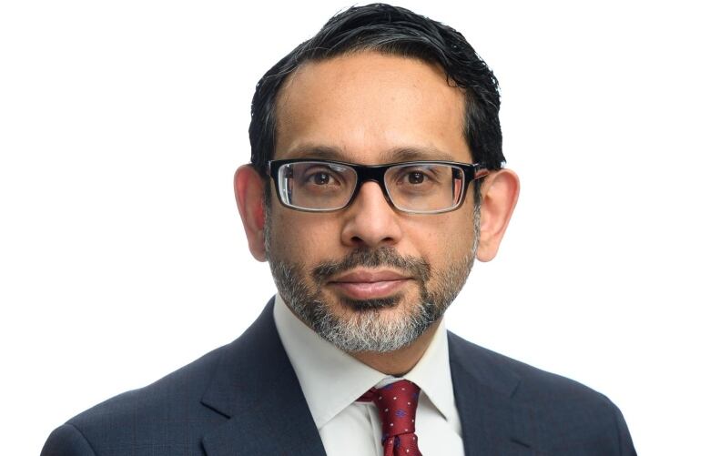 A portrait of a man in glasses, with a bread wearing a red tie and a suit with dark hair.