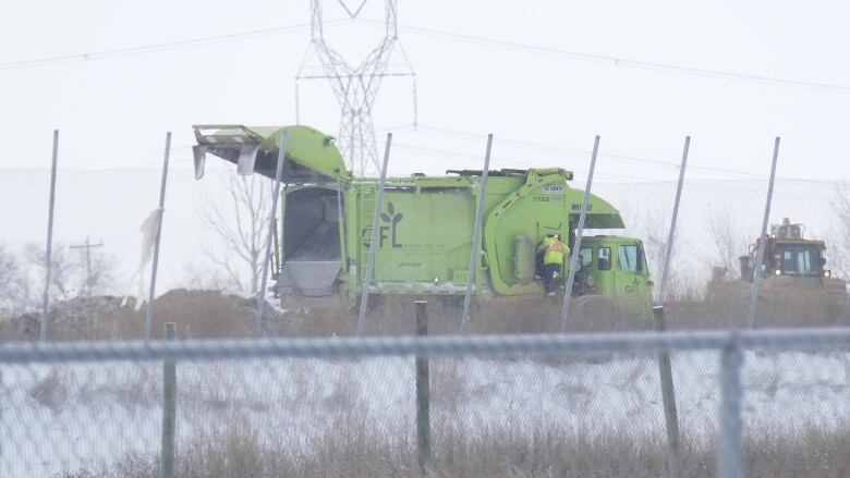 A dump truck is seen behind a chain-link fence on the property of a landfill.