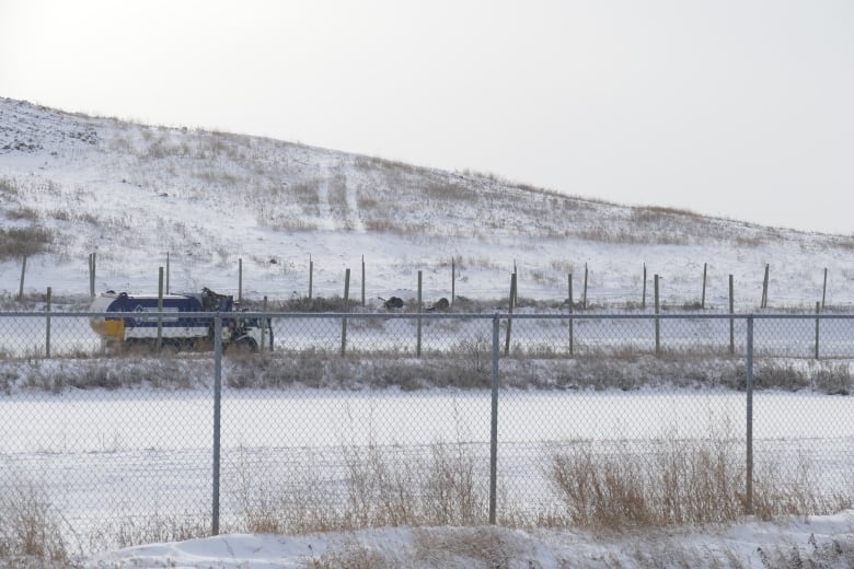 A garbage truck drives behind a fenced area covered in snow.