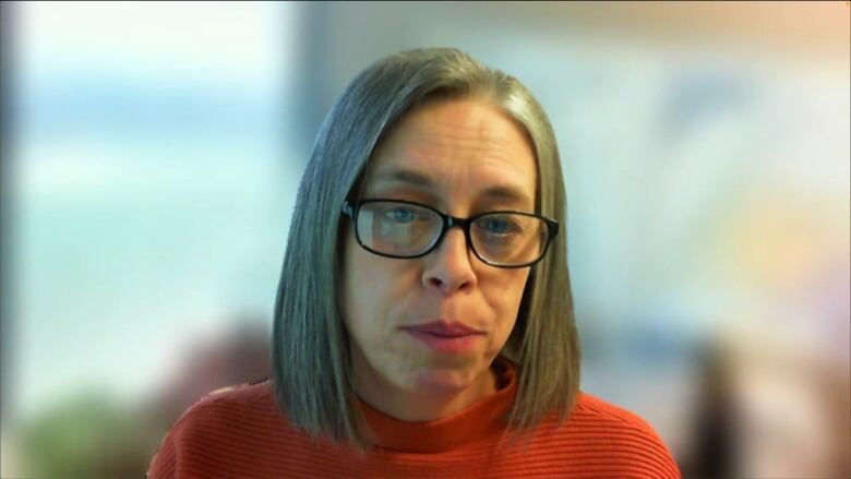 A woman wearing a red shirt looks into the camera.