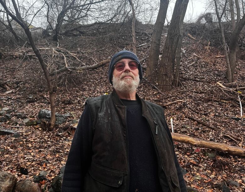 A man with a tuque and vest stands at the bottom of a ravine on a grey rainy day.