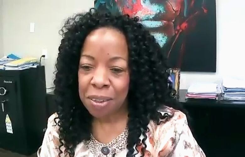 A woman with curly black hair wearing a white shirt with brown patterns