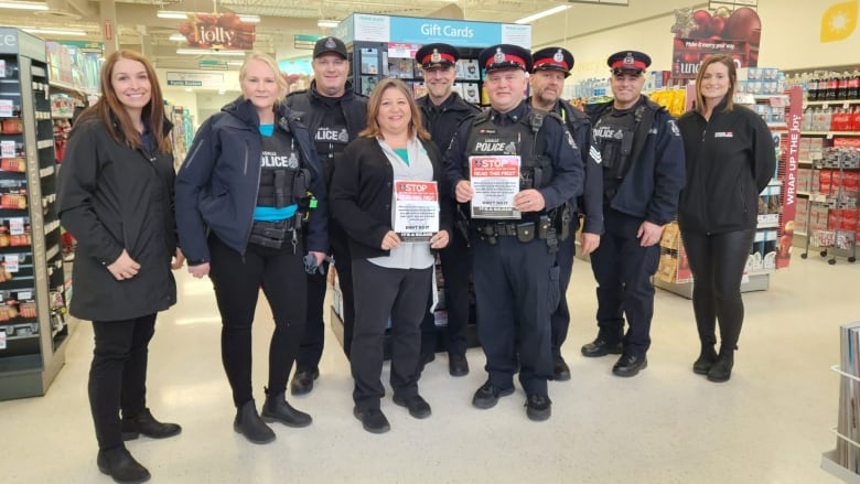 Police officers stand with workers in a store, holding up signs. 