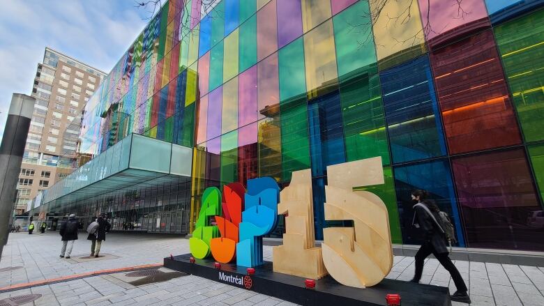 A large sign reads: COP15 in front of Montreal's palais des congres. A person walks past the sign. Trees in the photo are bare. 