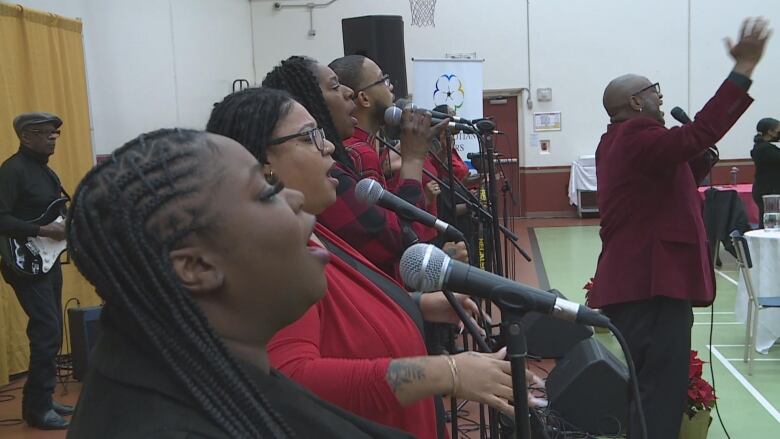 A row of people stand in front of mic while they sing