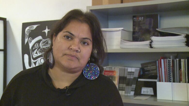 A woman wearing a black shirt and holiday earrings looks into the camera during an interview.