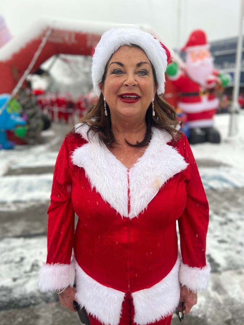 A smiling woman in a Santa suit on a snowy day. 