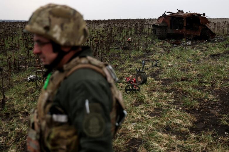 Individual wearing camoflage clothing and helmet with a tank in the background.