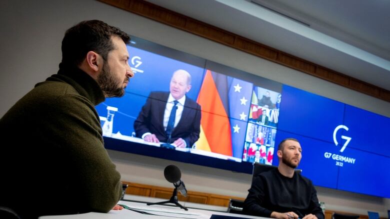 Leader of Ukraine in the foreground with a screen showing video feed from the G7 leaders summit. 