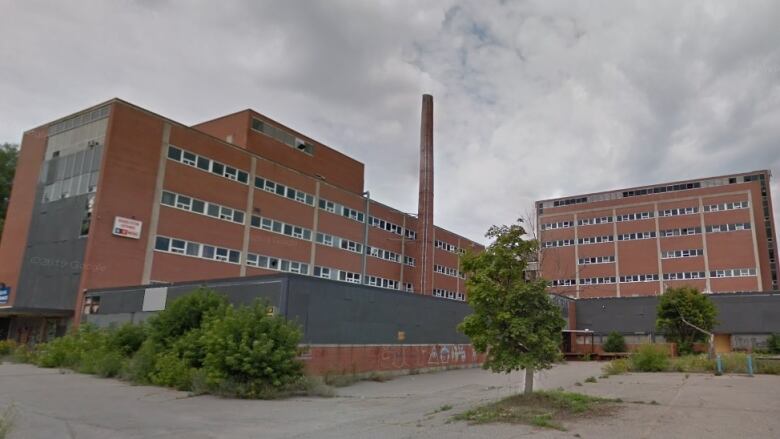 A large brick building with a smokestack is surrounded by scrub brush 