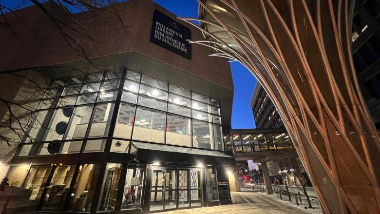 A photo shows the exterior of downtown Winnipeg's library branch at night. 